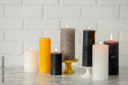 Different decorative wax candles on table against brick wall