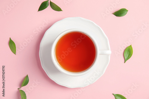 Cup of delicious tea with green leaves on color background, top view