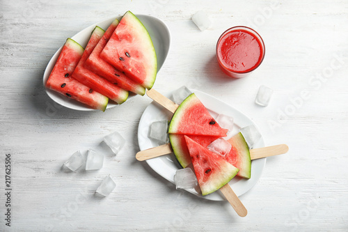 Flat lay composition with watermelon popsicles and ice cubes on white wooden background