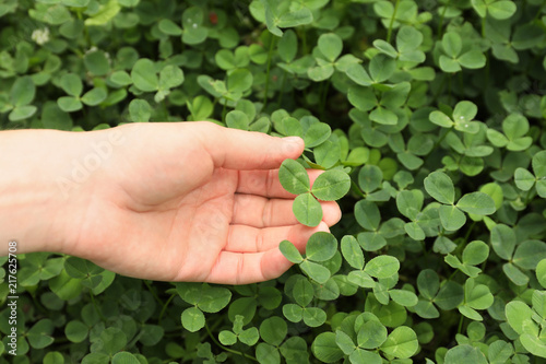 Woman holding four-leaf clover outdoors, closeup