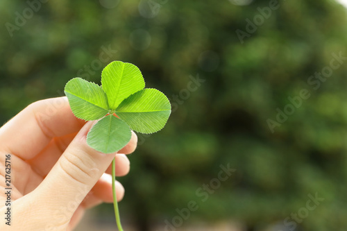 Woman holding four-leaf clover outdoors, closeup with space for text © New Africa