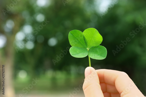 Woman holding four-leaf clover outdoors, closeup