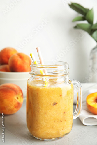 Tasty peach smoothie in mason jar and fresh fruit on table