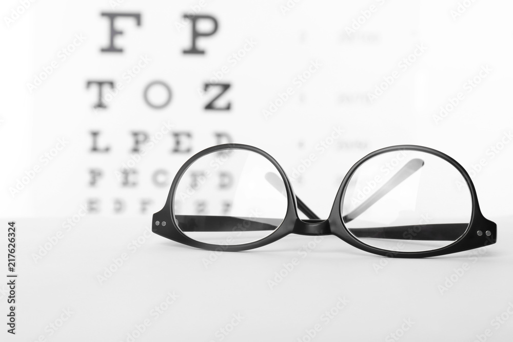 Glasses with corrective lenses on table against eye chart