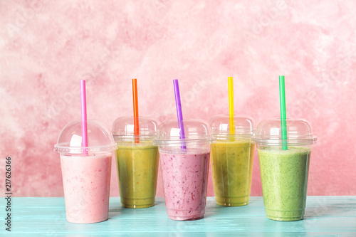 Plastic cups with smoothies on table against color background
