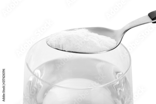 Spoon with baking soda over glass of water on white background