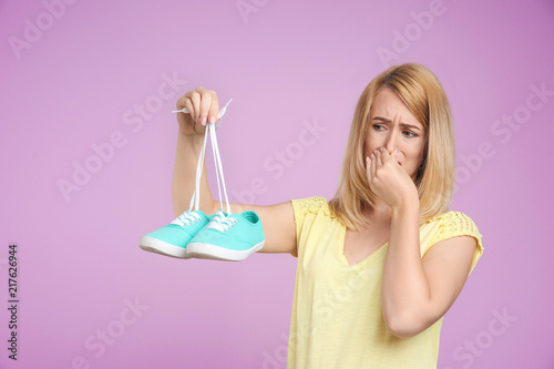 Young woman with stinky shoes on color background. Air freshener