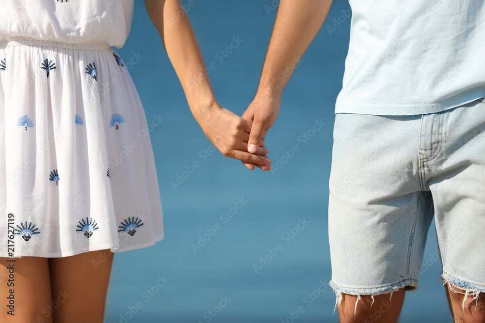 Happy young couple holding hands at beach on sunny day, closeup