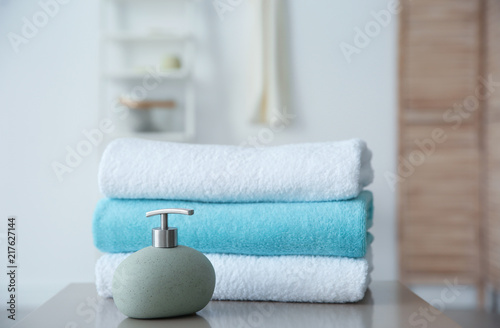 Clean towels and soap dispenser on table against blurred background