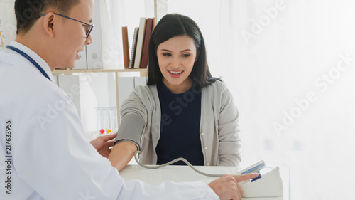 Canvas Print Professional doctor wearing white coat is checking woman patient with stethoscope and measure blood pressure in hospital background