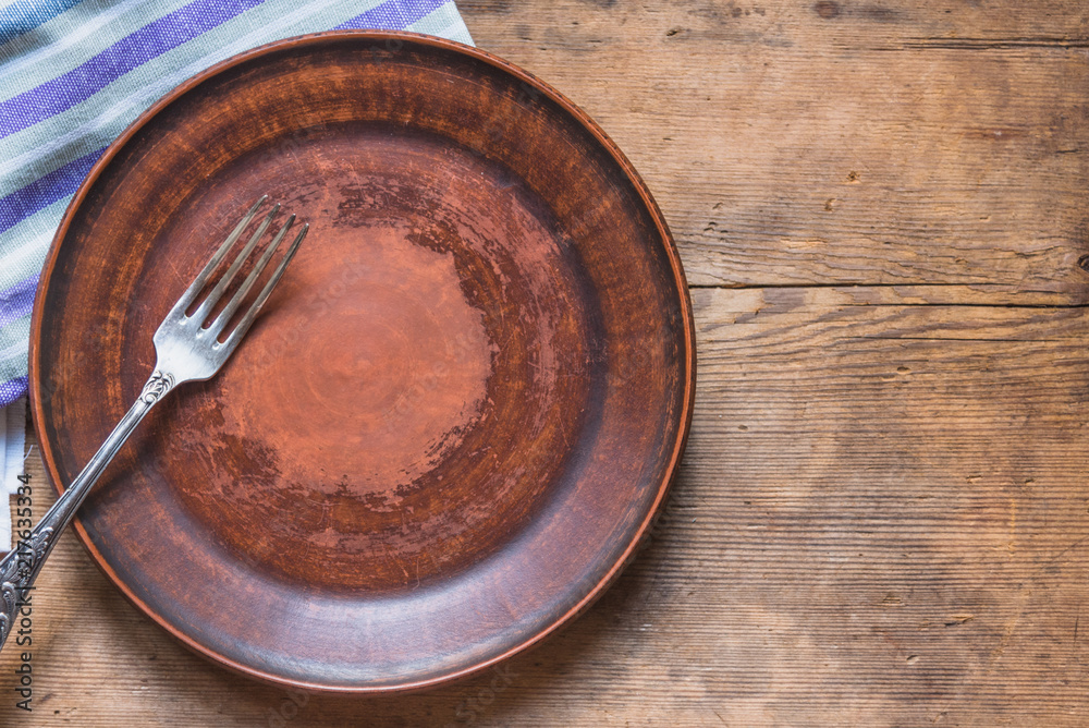 Empty clay plate with a fork on an old wooden table, top view, copy space Empty clay plate with a fork on an old wooden table, top view, copy space