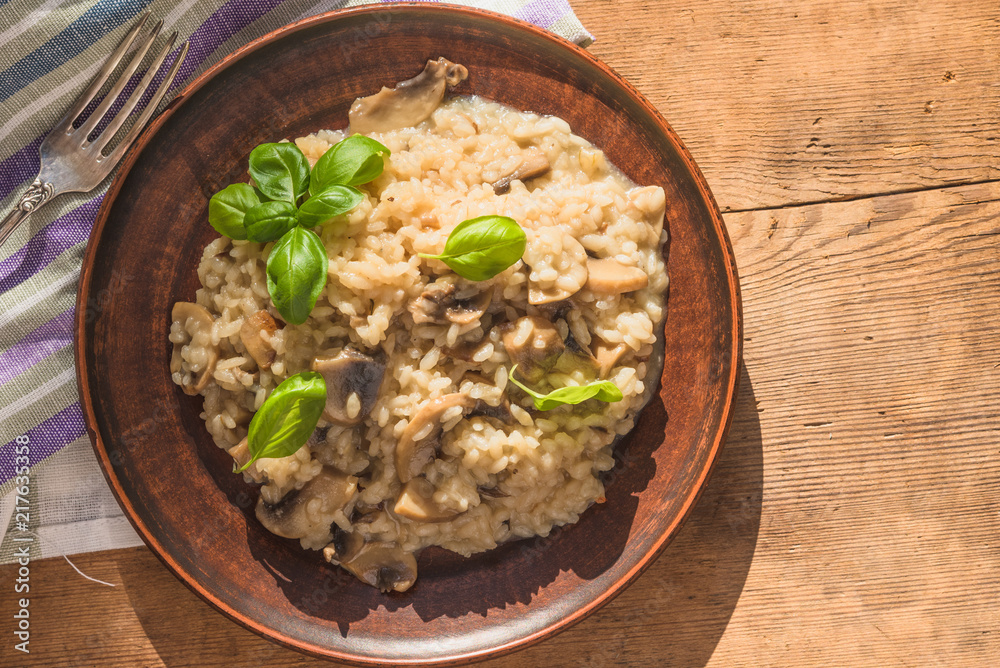 Italian traditional dish - risotto with mushrooms with basil leaves in a clay plate on an old wooden table, top view, copy space for a recipe Italian traditional dish - risotto with mushrooms with basil leaves in a clay plate on an old wooden table, top view, copy space for a recipe
