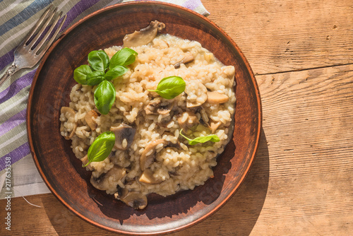 Italian traditional dish - risotto with mushrooms with basil leaves in a clay plate on an old wooden table, top view, copy space for a recipe