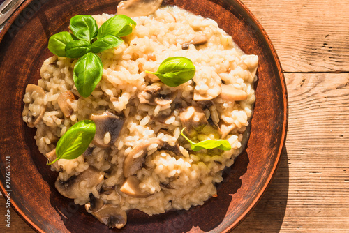 Italian traditional dish - risotto with mushrooms with basil leaves in a clay plate on an old wooden table, top view, copy space for a recipe