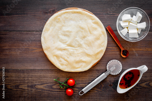 Fototapeta Naklejka Na Ścianę i Meble -  Process of cooking pizza. Pizza Margarita. Raw dough and filling. Cherry tomatoes, cheese mozzarella, spices near knife for pizza on dark wooden background top view mockup copy space