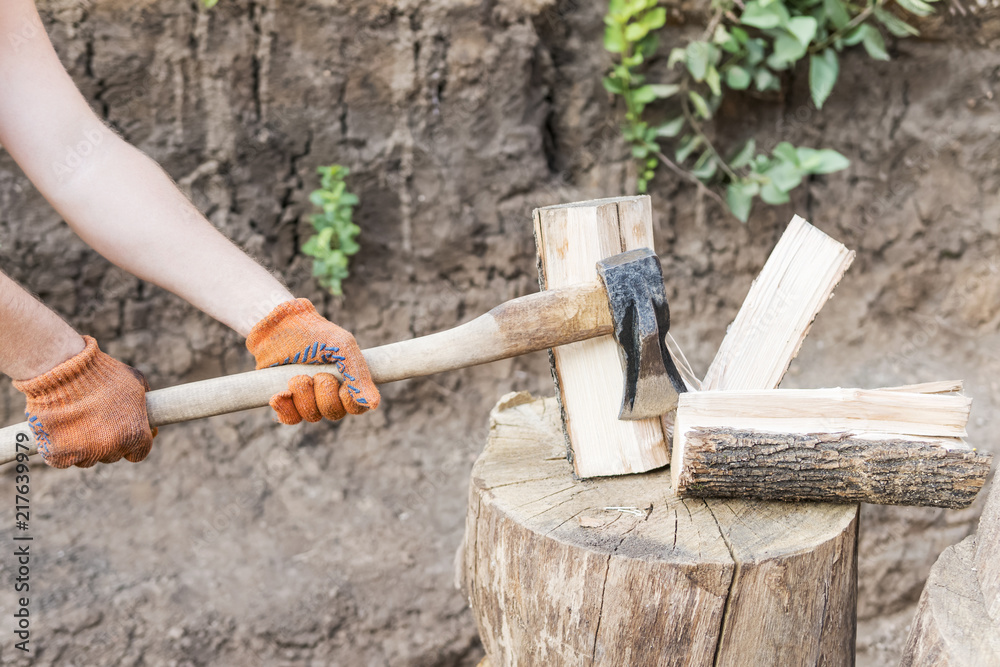Male hands in orange gloves cut a log with a cleaver, close-up Male hands in orange gloves cut a log with a cleaver, close-up