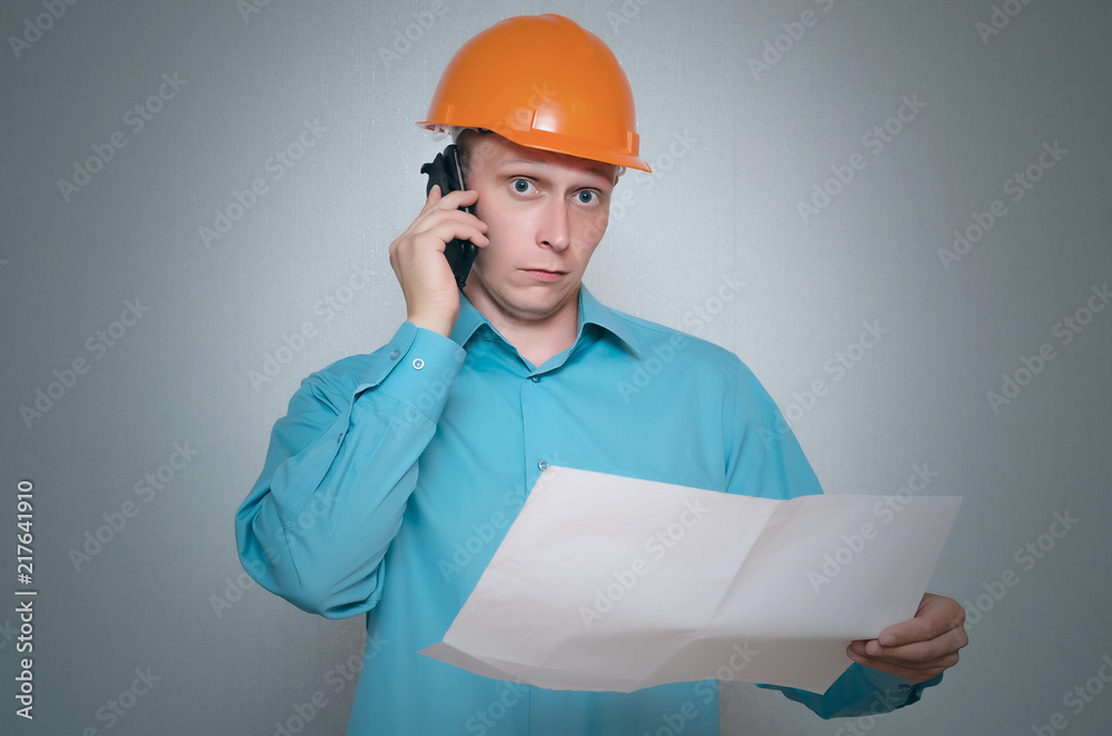 Builder construction worker with mobile phone is holding in hand a plan draft document isolated on gray background. Builder construction worker with mobile phone is holding in hand a plan draft document isolated on gray background.