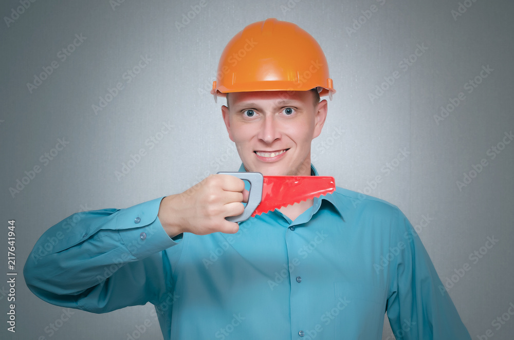 Happy builder worker with hand saw tool in hands isolated on gray background.