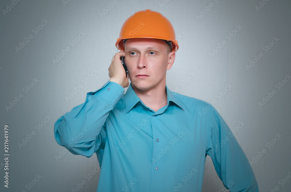 Builder worker is talking on mobile phone isolated on gray background.