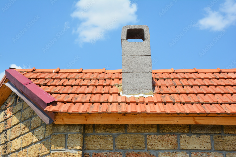 Installing chimney on house construction with red clay roof and limestone wall.