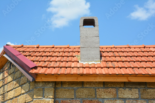 Installing chimney on house construction with red clay roof and limestone wall.