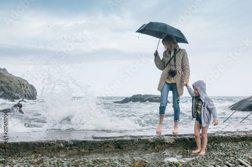 Mother with child - little boy on a stony beach in bad weather on the beach, the ocean. Walk along the coast. Waves beat against the shore.