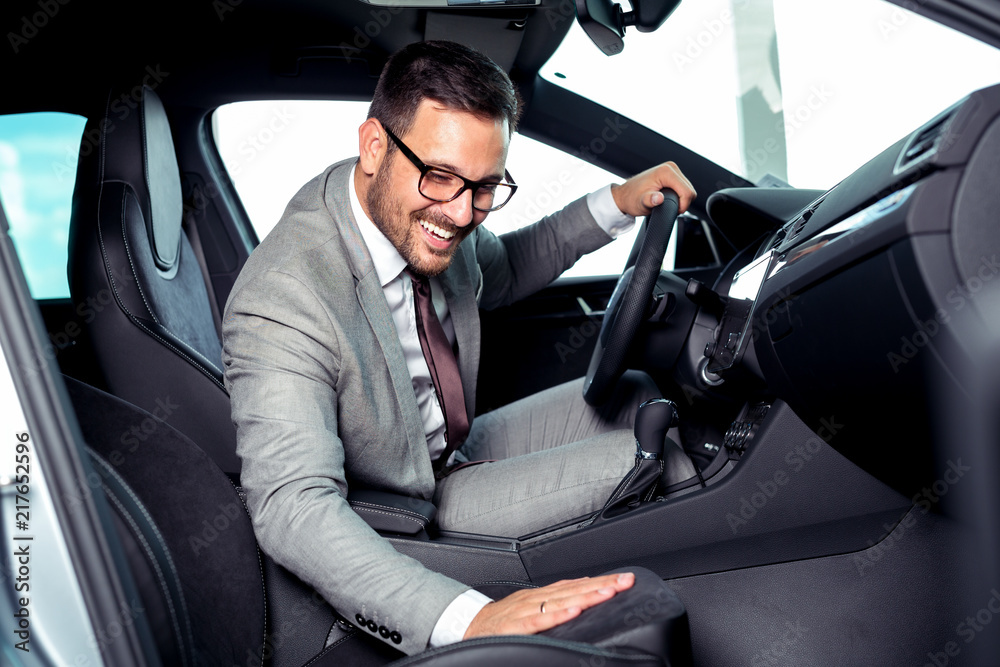 Handsome businessman is sitting in a new car in car dealership