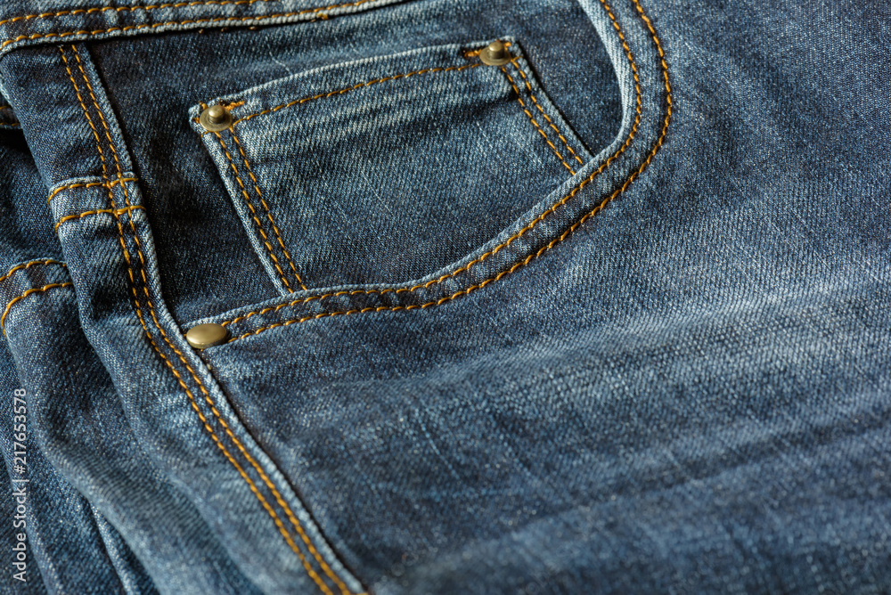 Close-up of a piece of blue jeans with orange stitches. Pocket with rivets close-up. Close-up of a piece of blue jeans with orange stitches. Pocket with rivets close-up.