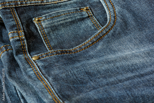 Close-up of a piece of blue jeans with orange stitches. Pocket with rivets close-up.