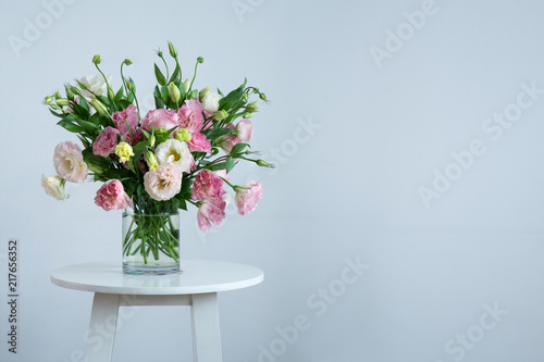 still life of white and pink Lisianthus in clear glass vase on small round table isolated on light gray background