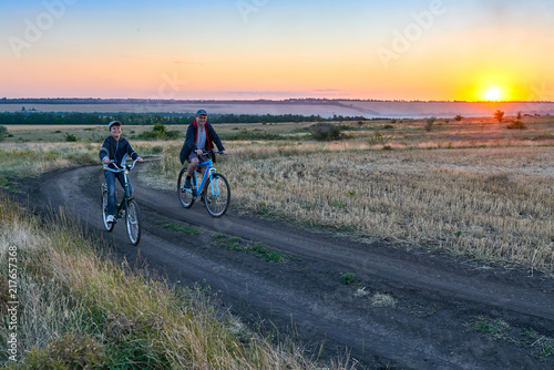 father and son ride a bike in the country on the field in the evening