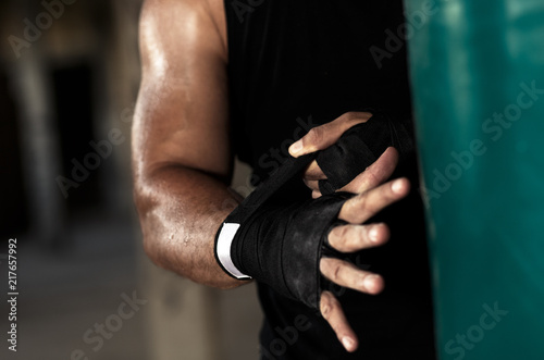 Male boxer bandage his hands before punching a boxing bag in warehouse.