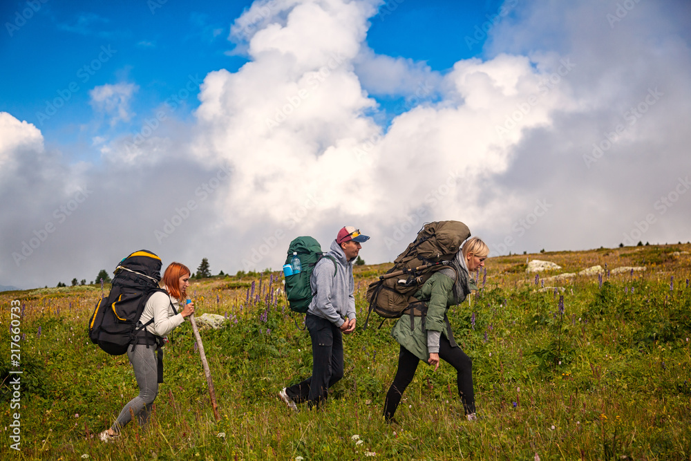 Travel Lifestyle and survival concept rear view. Two hiking women and man with backpack go along the path to the mountains in a long hike on a warm summer day, a back view. . Travel Lifestyle and survival concept rear view. Two hiking women and man with backpack go along the path to the mountains in a long hike on a warm summer day, a back view. .