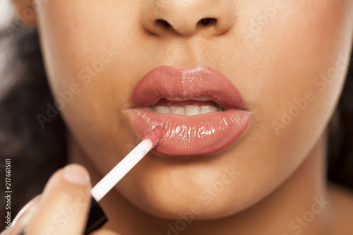 closeup of a young dark-skinned woman applying lipgloss with brush on a white background