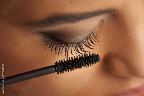 closeup of a young dark-skinned woman applying mascara on a white background photo