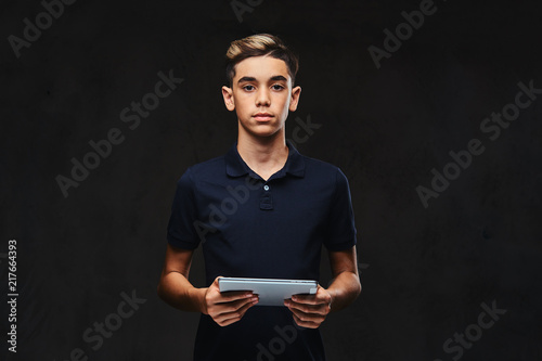 Handsome young guy dressed in a black t-shirt holds a tablet computer. Isolated on the dark background.