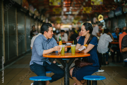 Portrait of a good looking Chinese Asian couple having a date at a hawker center during the weekend in Singapore. Both are enjoying their sugarcane juice and fried bananas.