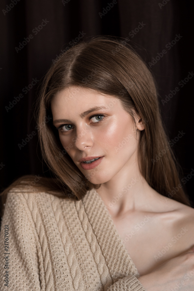 Portrait of a girl with natural make-up and bare shoulder. Brown background. Knitted sweater from the shoulder. Long smooth hair. Portrait of a girl with natural make-up and bare shoulder. Brown background. Knitted sweater from the shoulder. Long smooth hair.