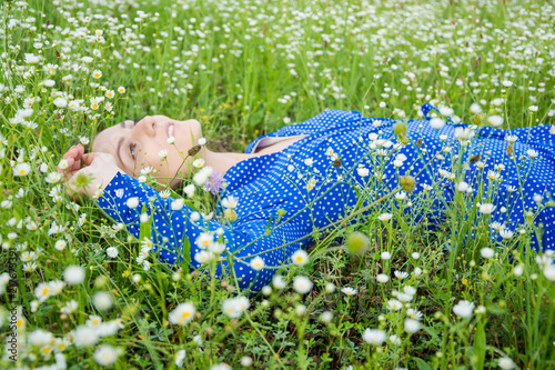 Portrait of a beautiful young woman lies among white wildflowers in a meadow and looks up