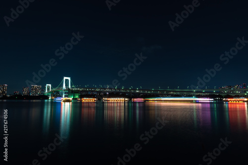 Suspension bridge at night The light from the ship and the building from the city. With reflection in water
