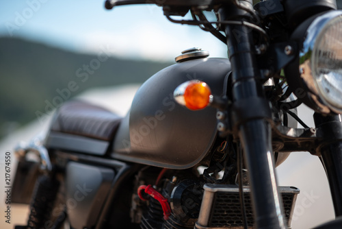 Side of the motorcycle classic black. There are many parts blurred by the sky and mountains.