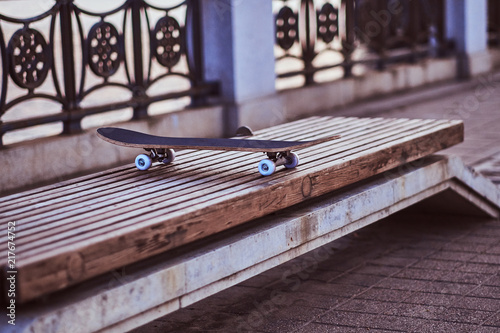 Close-up photo of a skateboard that standing on a bench on the embankment during beautiful sunset.