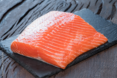 Fresh salmon fillet on black cutting board.