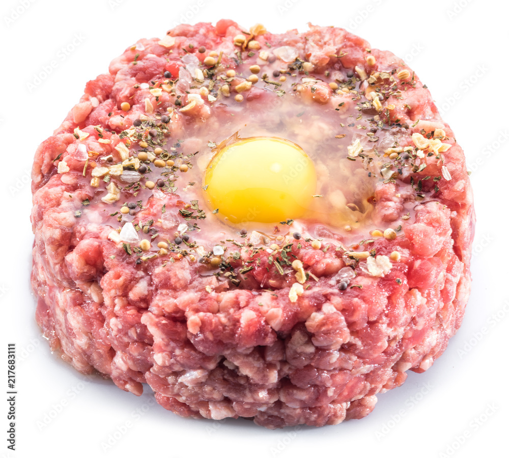 Ground cutlet or raw hamburger with quail egg yolk and seasonings on white background. Top view. Ground cutlet or raw hamburger with quail egg yolk and seasonings on white background. Top view.