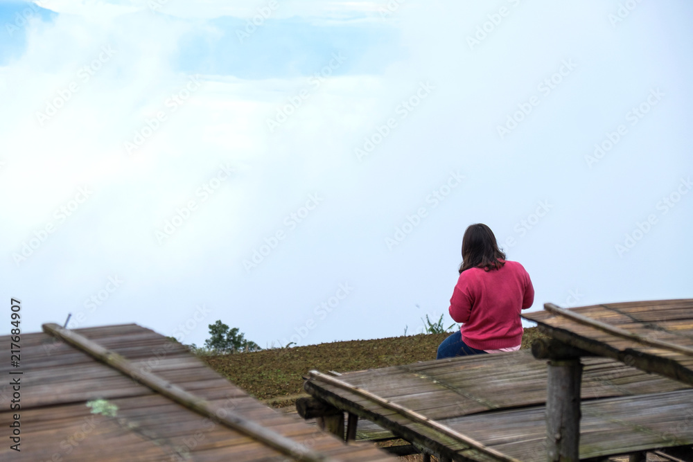 A woman with pink shirt sitting at the big wooden chair with clouds background