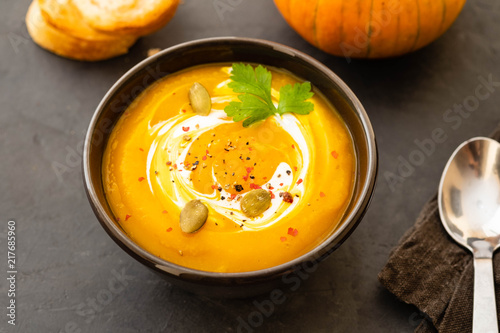 Pumpkin soup in a bowl with fresh pumpkins, garlic and parsley herbs on a black background. Autumn concept.