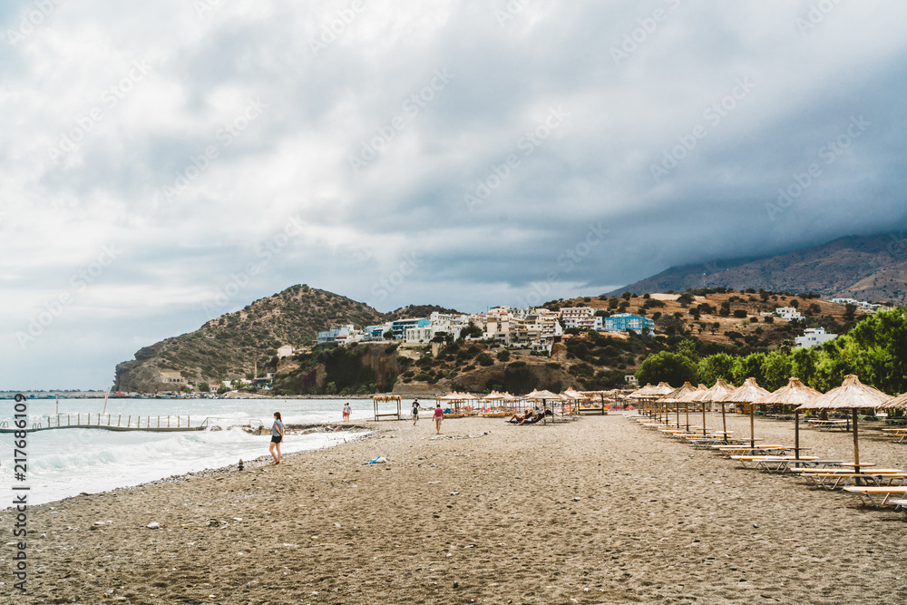 Crete, Greece. View from cliffs to village with marine vessels, boats and lighthouse. View from cliff on Bay with beach and architecture - vacation destination resort with clear ocean water. Rethymno