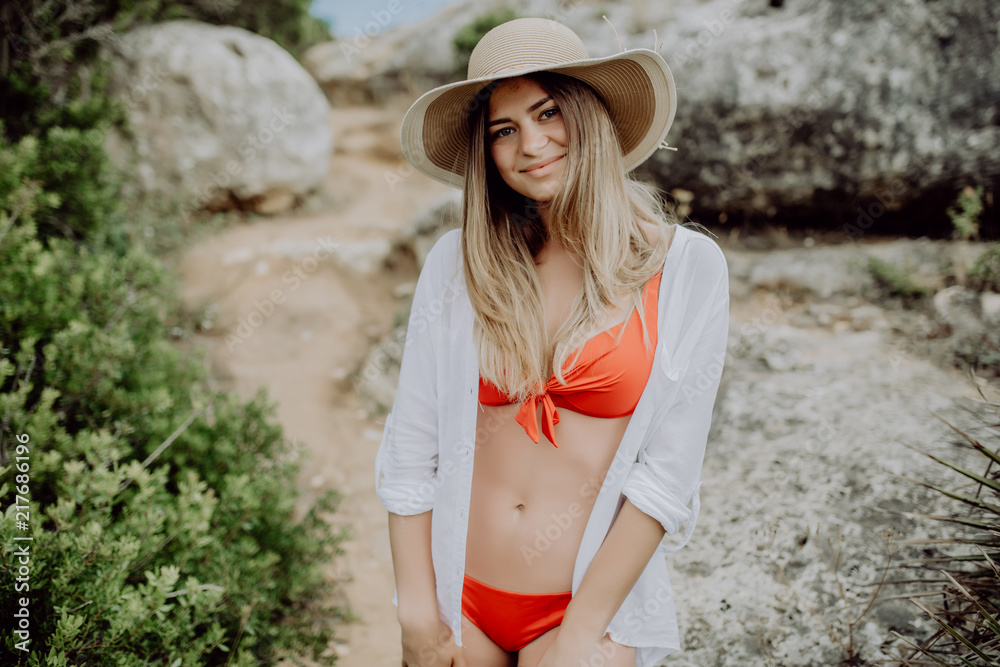 Beautiful young wearing white shirt over swimsuit and straw hat posing on beach in sunlight Stock Photo | Adobe Stock