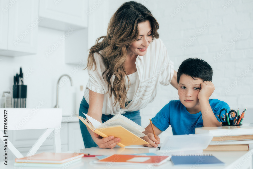 portrait of mother helping bored son with homework at home portrait of mother helping bored son with homework at home