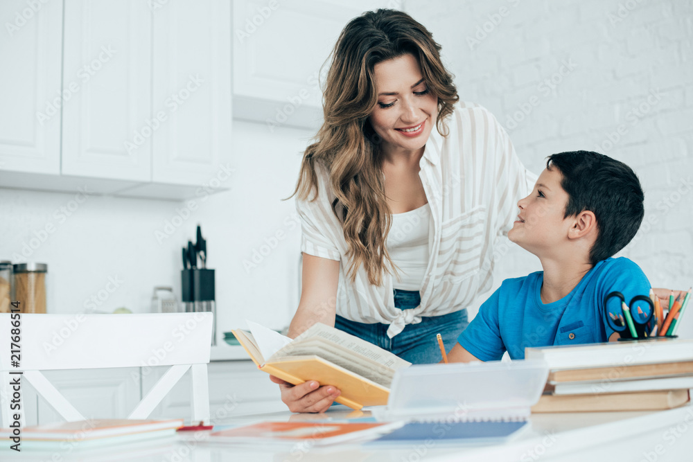 portrait of smiling mother helping son with homework in kitchen at home portrait of smiling mother helping son with homework in kitchen at home